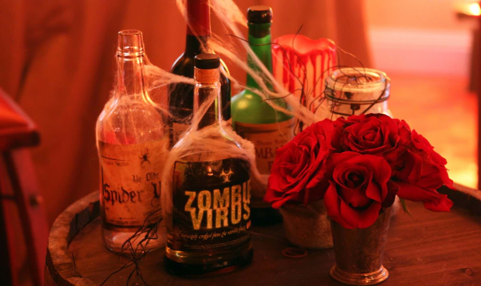 alcohol bottles covered in decorative spider webs next to red roses