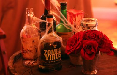 alcohol bottles covered in decorative spider webs next to red roses