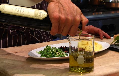 Jordan Winery extra virgin olive oil being poured into beaker with chopped ingredients on plate in background