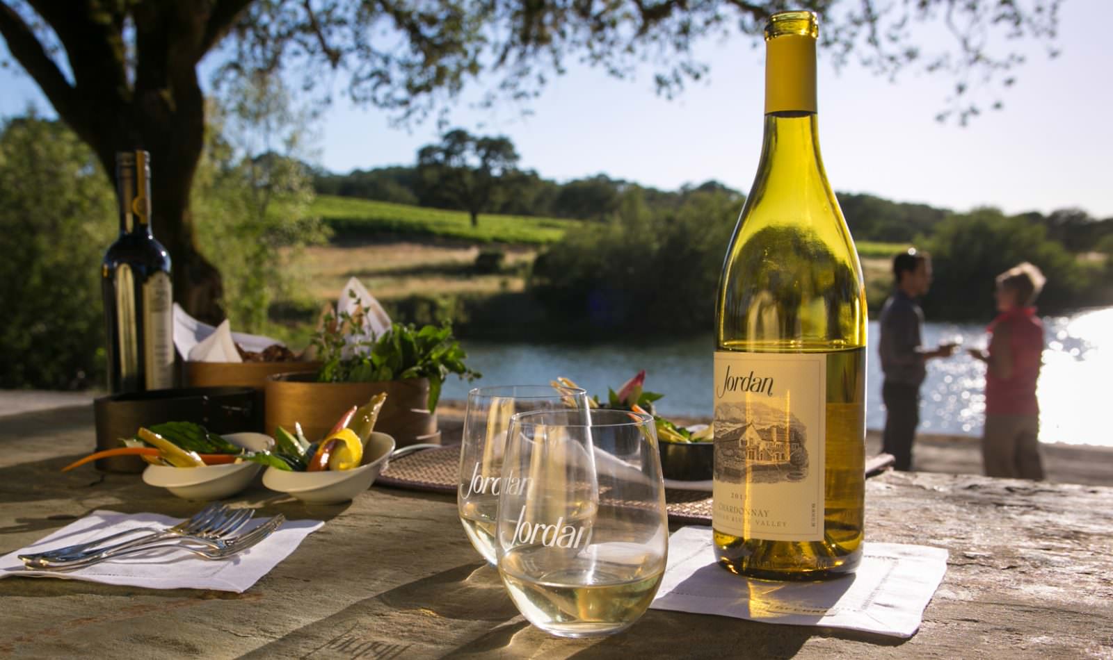 bottle of Jordan Winery Chardonnay with two logo glasses and bites of food on the Jordan Winery property