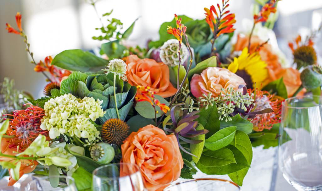 A close up of a floral arrangement with ornamental cabbage, smooth hydrangea, orange spray roses and orange flame calla lily.