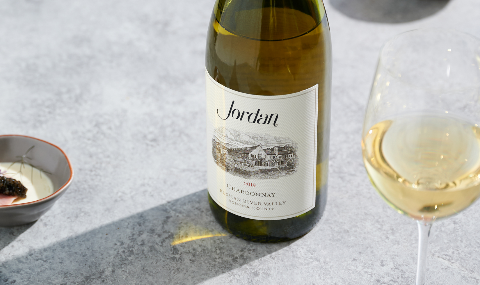 chardonnay wine bottle with wine glass on marble background