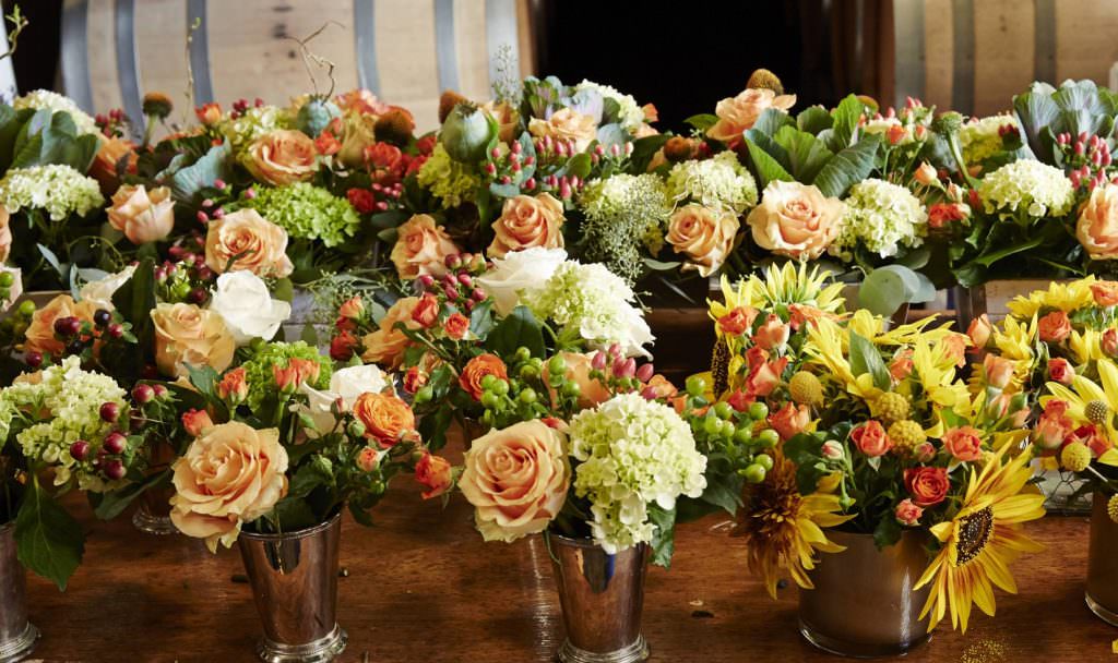 An assortment of floral centerpieces with ornamental cabbage, smooth hydrangea, orange spray roses and orange flame calla lily.