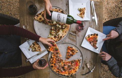 overhead shot of two people sitting at a table with pizza and Jordan winery Cabernet being poured into a glass