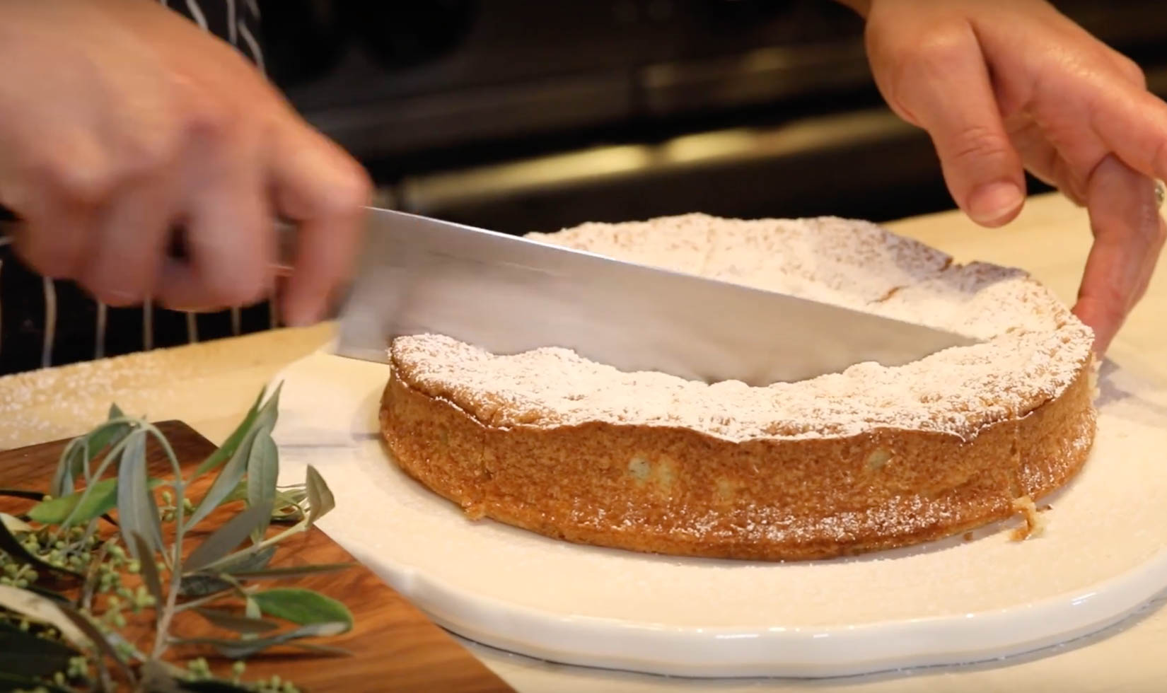 knife cutting into olive oil cake with powdered sugar