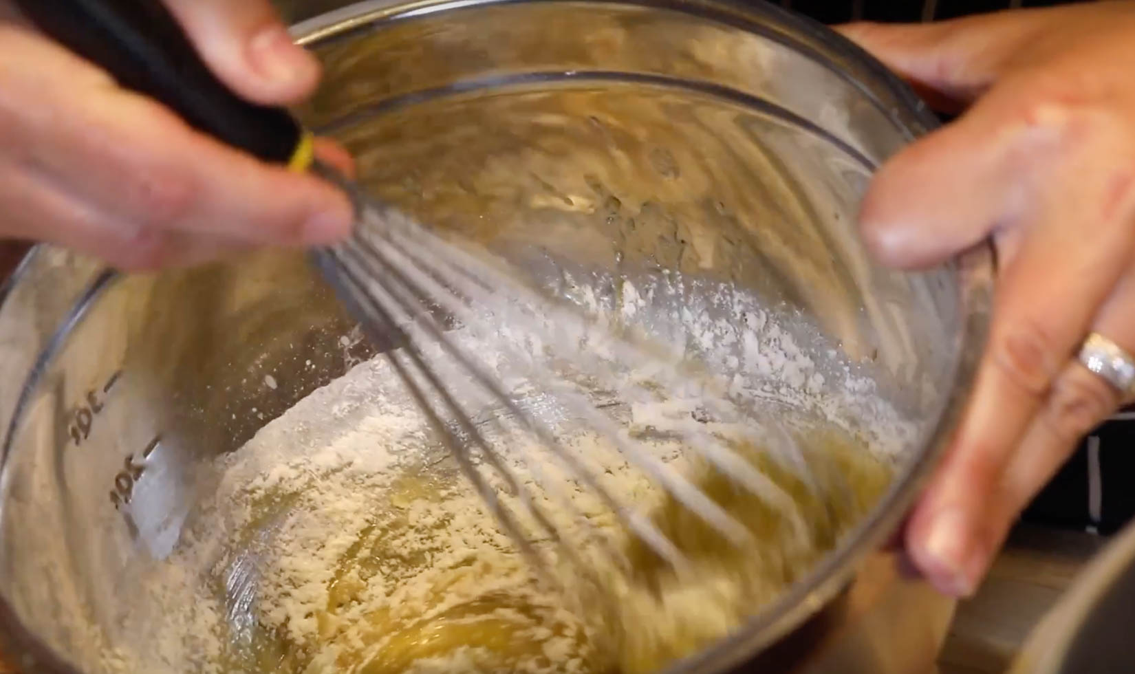 hands whisking cake flour into olive oil batter in mixing bowl