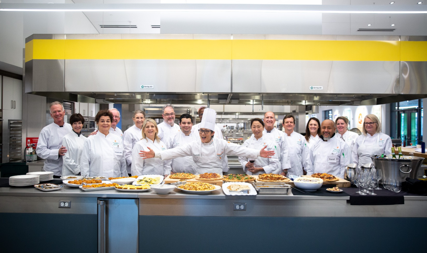 Group cooking class in commercial kitchen with everyone in white uniforms. 