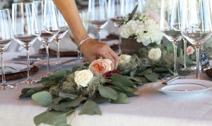 hand adjusting a eucalyptus garland table runner on a dining table