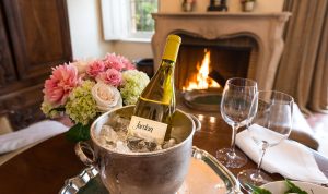 bottle of Jordan Chardonnay on ice next to wine glasses with fire burning in fireplace in background in a Jordan Winery suite