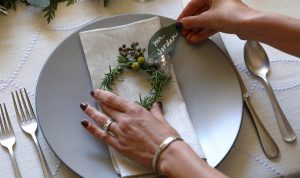 hands adjusting a rosemary wreath with a leaf name tag at a holiday table setting