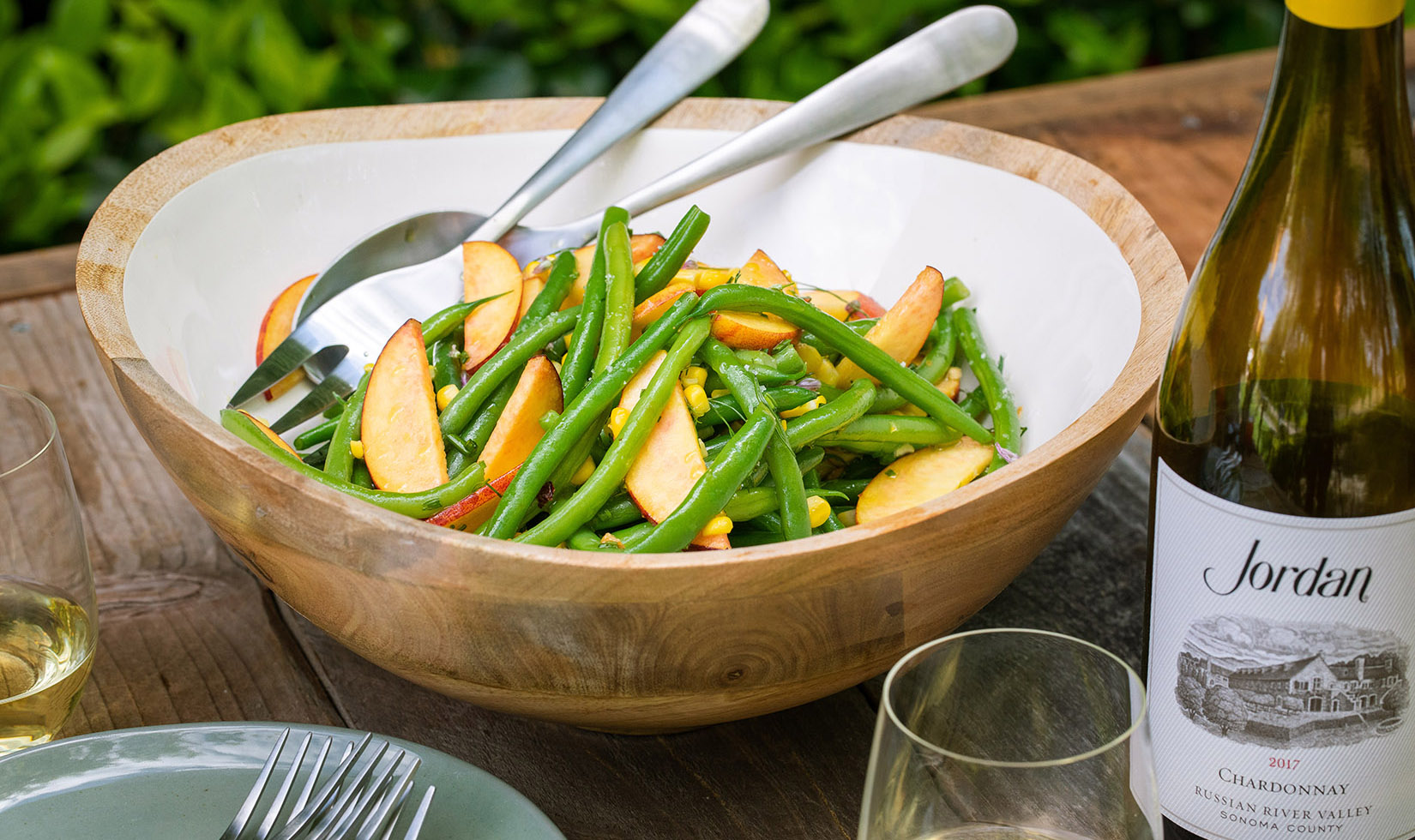 French green bean salad with peaches in bowl next to a bottle of Jordan Chardonnay