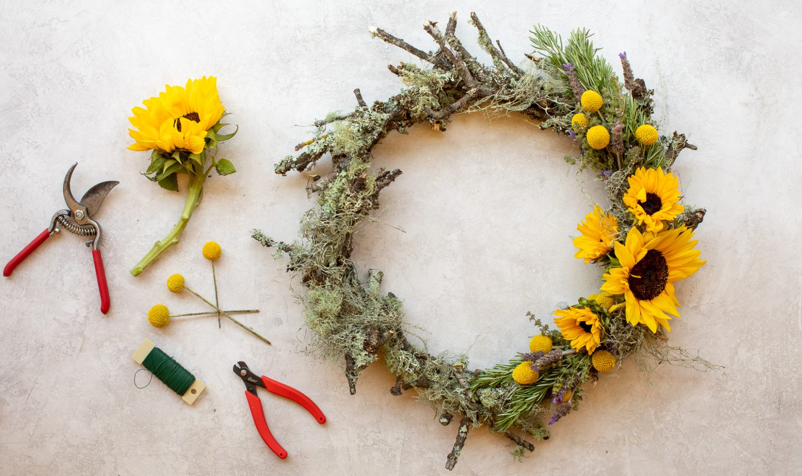 summer Oak wreath with moss and sunflowers next to gardening sheers, a sunflower, thread and billy balls