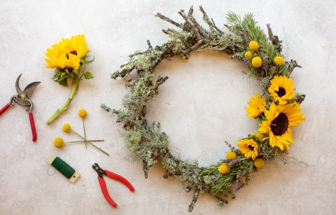 summer Oak wreath with moss and sunflowers next to gardening sheers, a sunflower, thread and billy balls