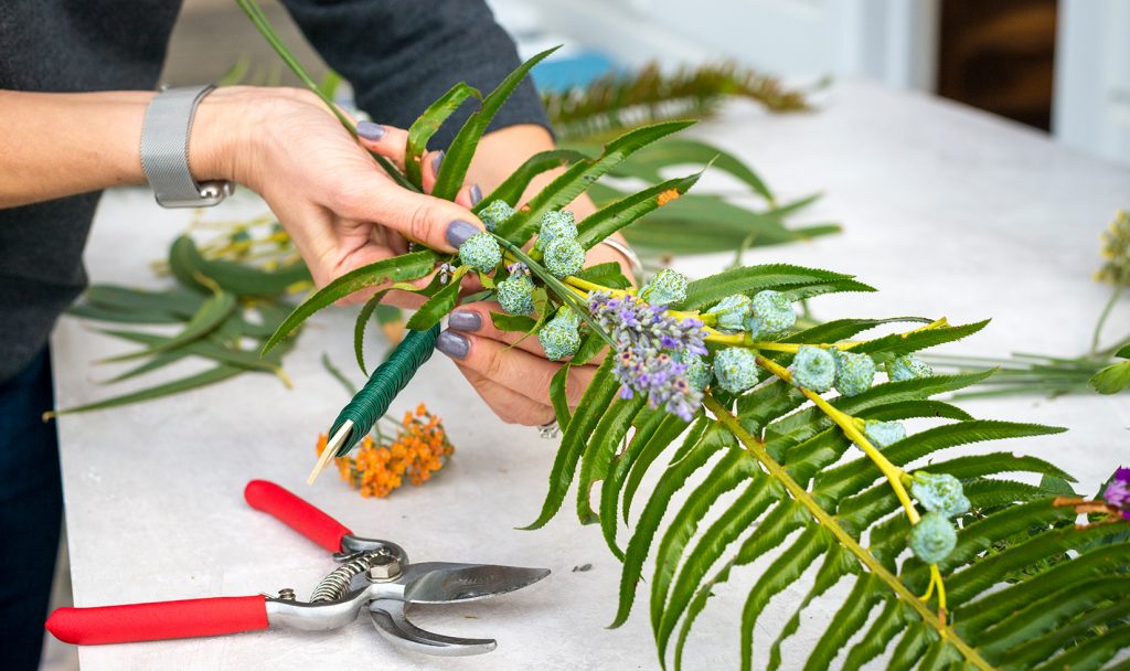 Close-up image of hands wrapping floral wire around green fronds for a table garland.