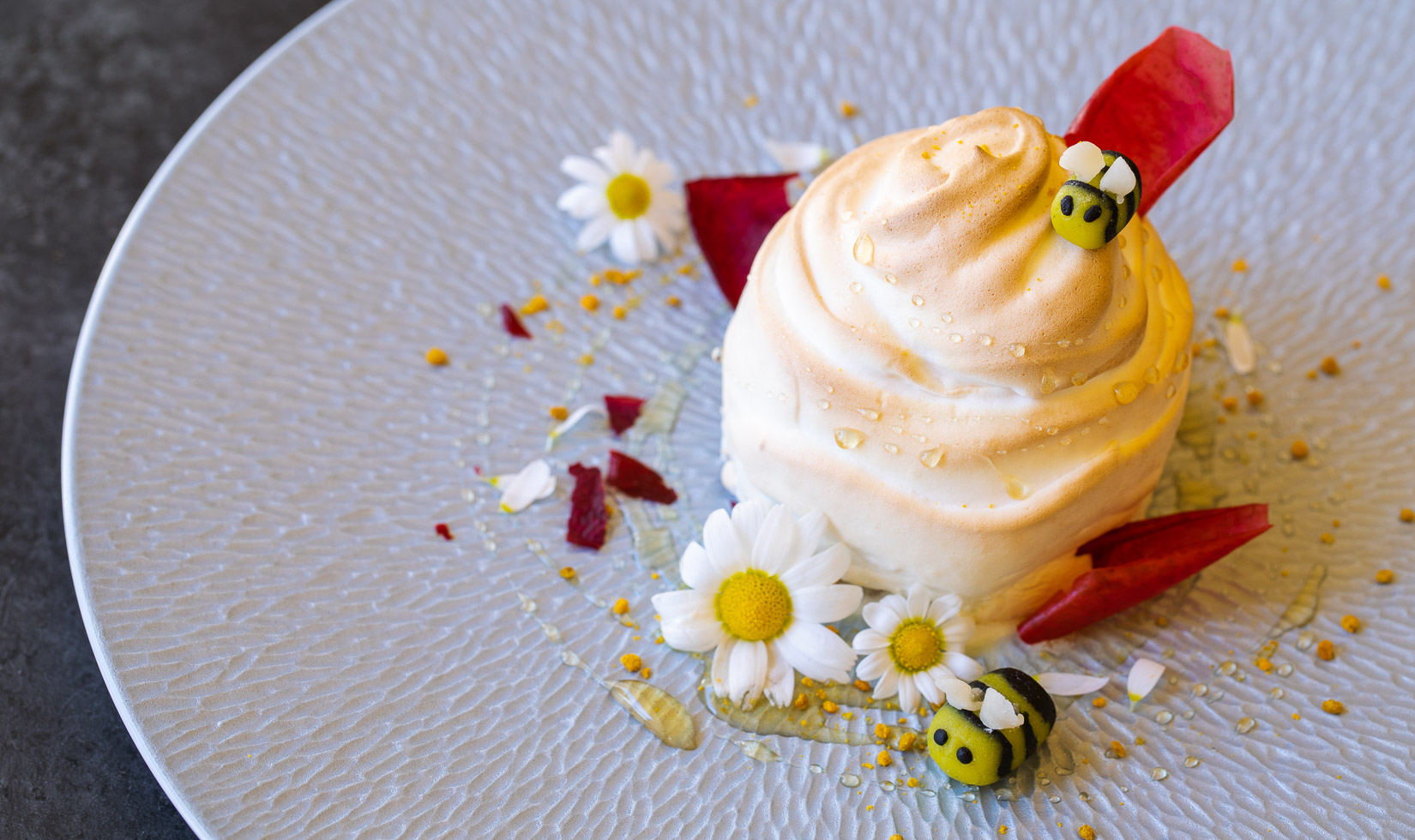 Baked Alaska dessert with marizpan bees and edible flowers on blue plate