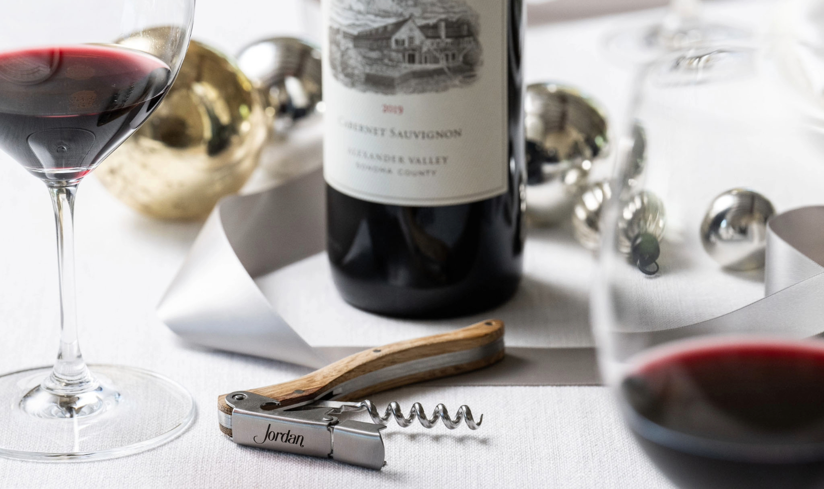 corkscrew with wooden handle in front of bottle of cabernet sauvignon on table decorated with christmas ornaments 