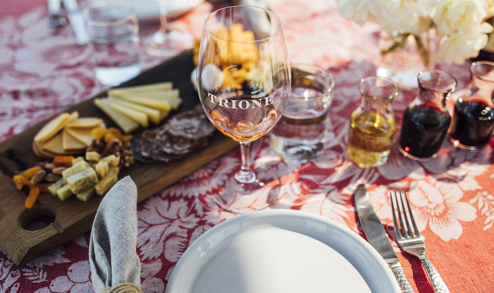 table setting with orange tablecloth, white plate, wine glass etched with Trione and cheese plate
