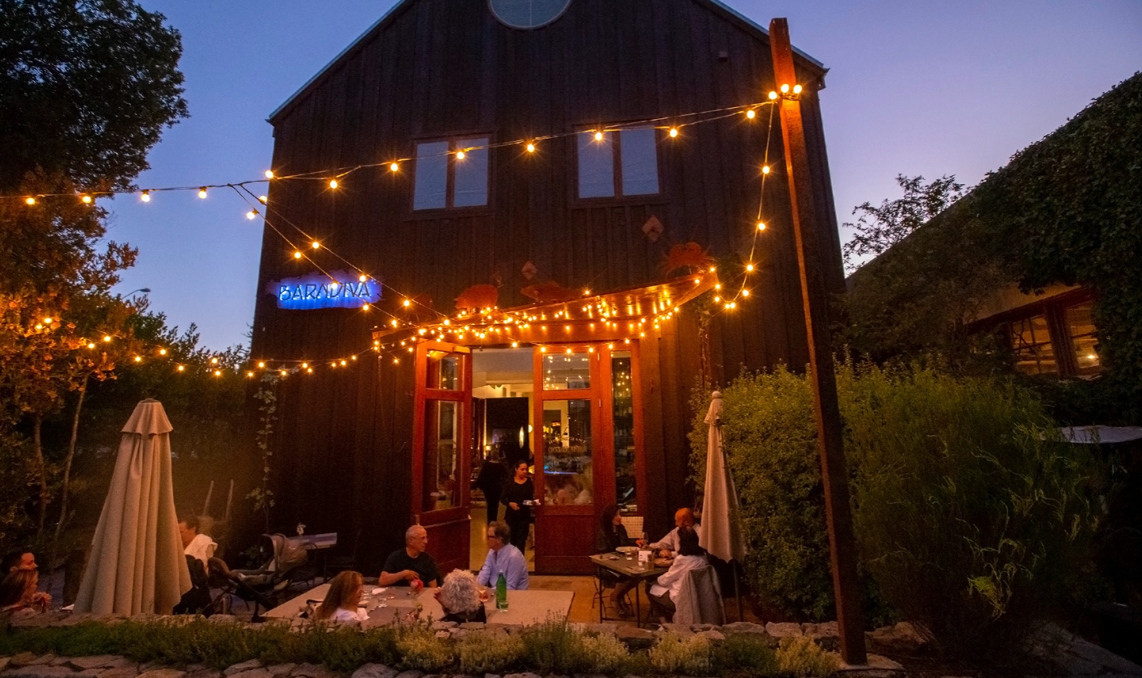 diners sitting around outdoors tables in front of restaurant styled as a traditional red barn