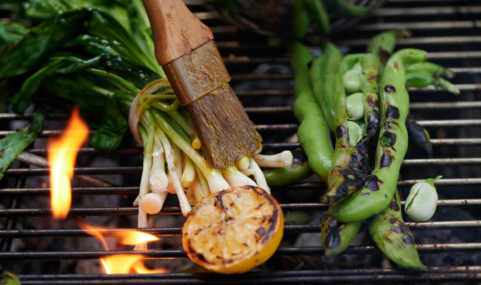 Green vegetables on a grill being brushed with oil