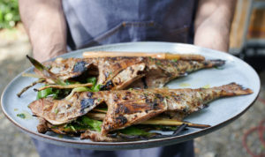 person holding plate of two grilled fish fillets