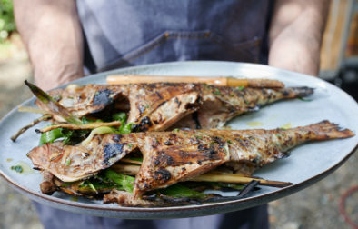 person holding plate of two grilled fish fillets