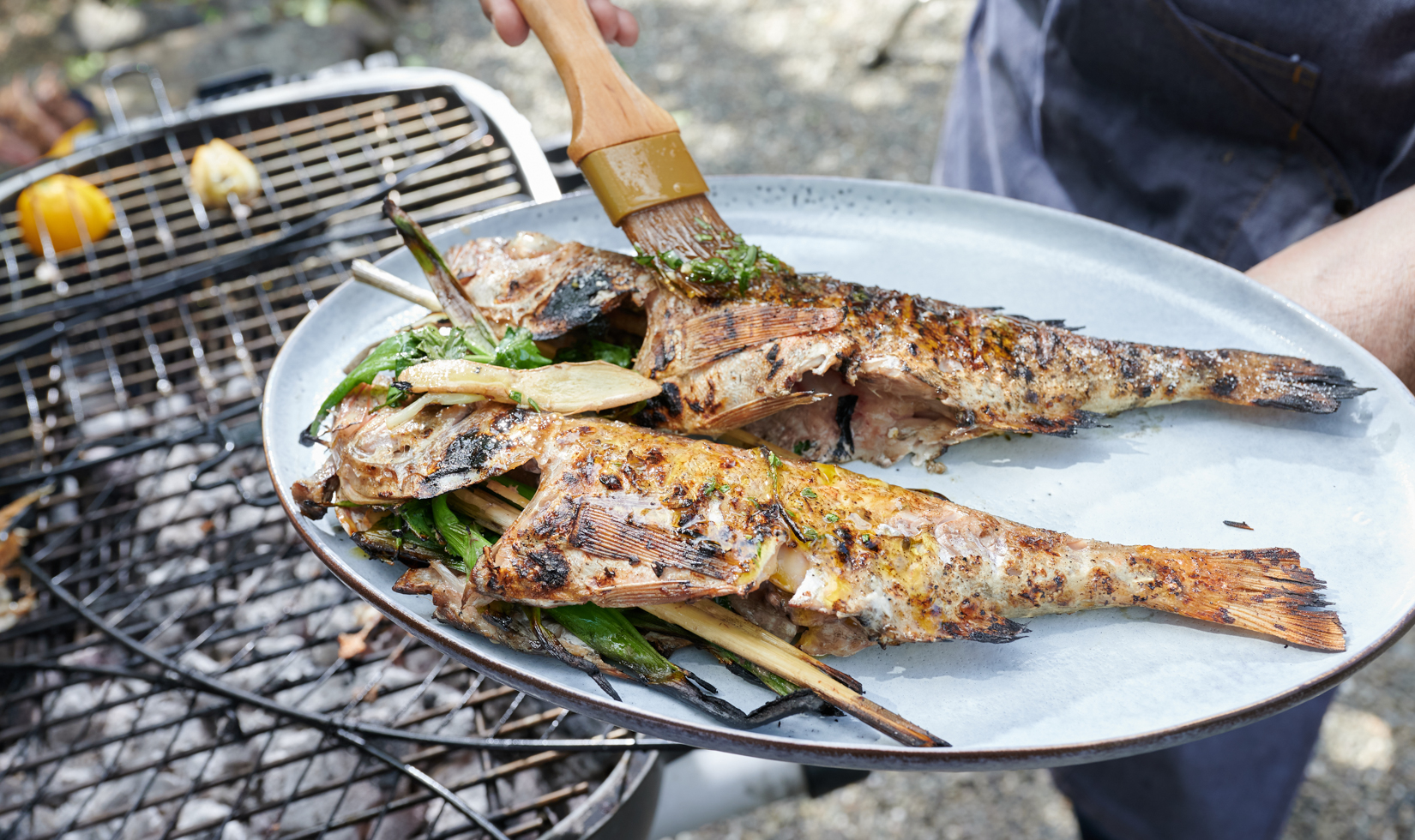 brushing two fish with marinade over the grill