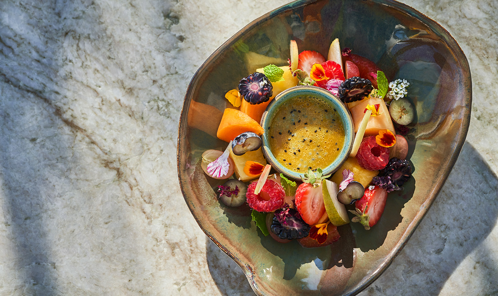 bowl of colorful fruit with edible flowers and dip