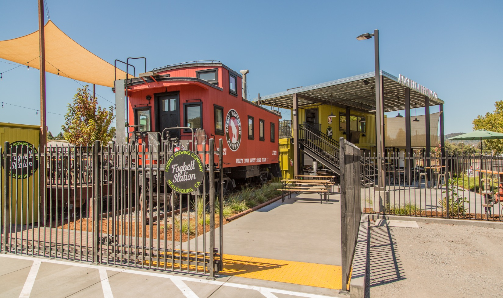 Exterior of Fogbelt station with red train caboose structure next to wooden deck with seating. 