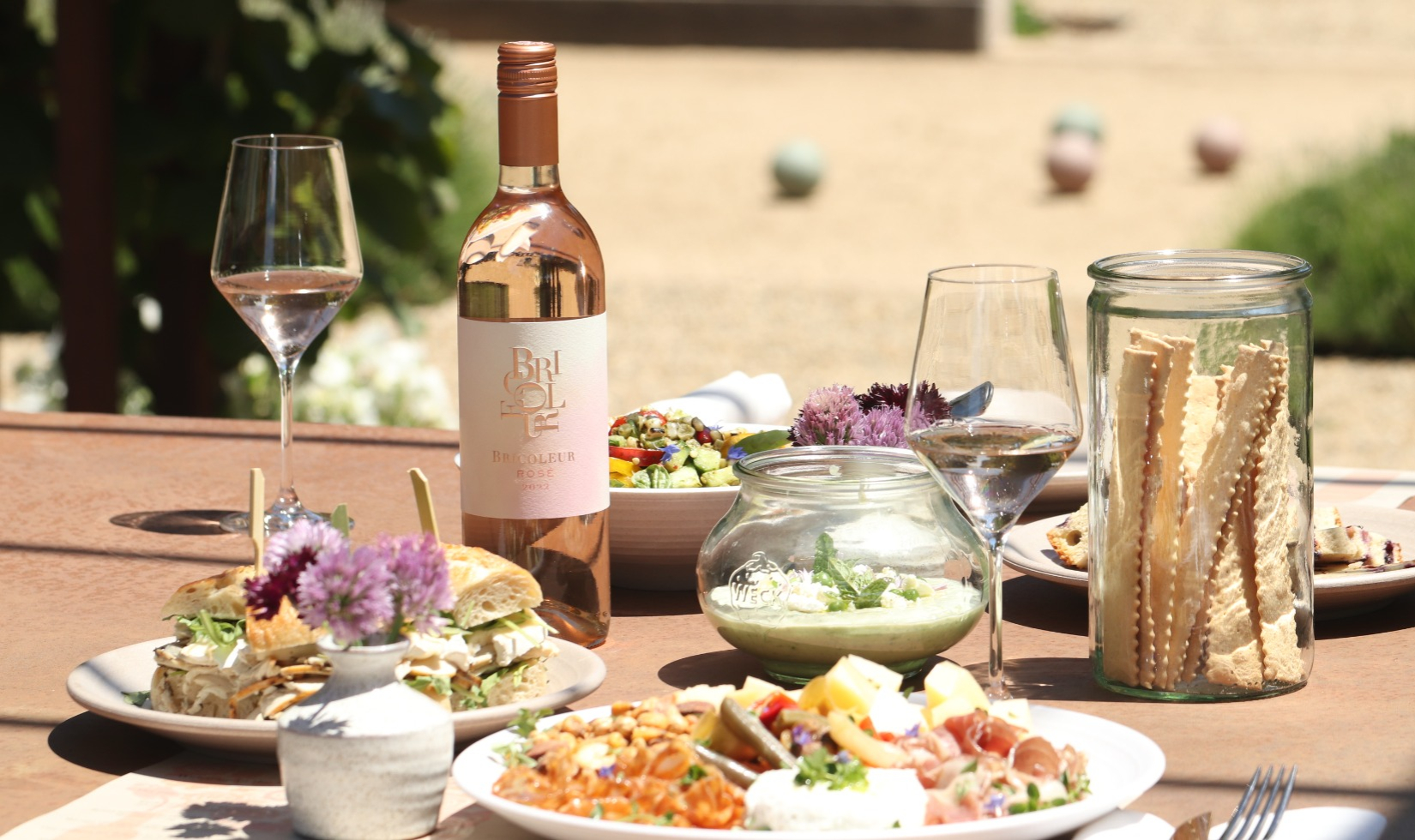 Outdoor table with a variety of dishes paired with glass of rose 