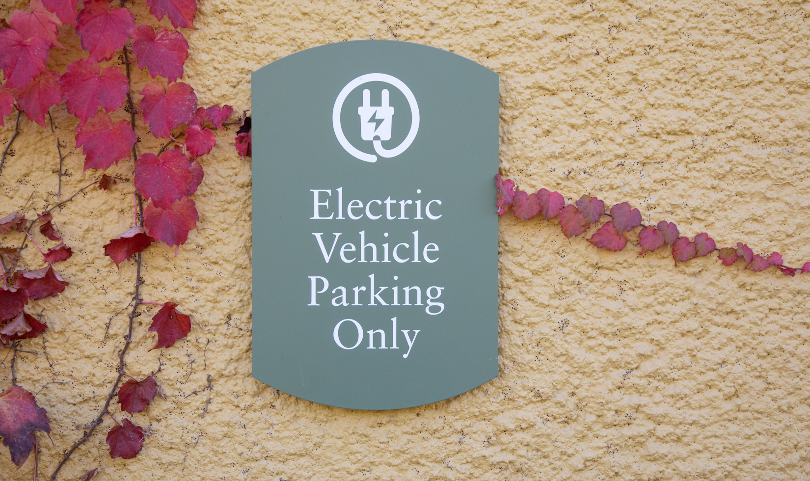 electric vehicle charging sign posted on yellow wall with boston ivy