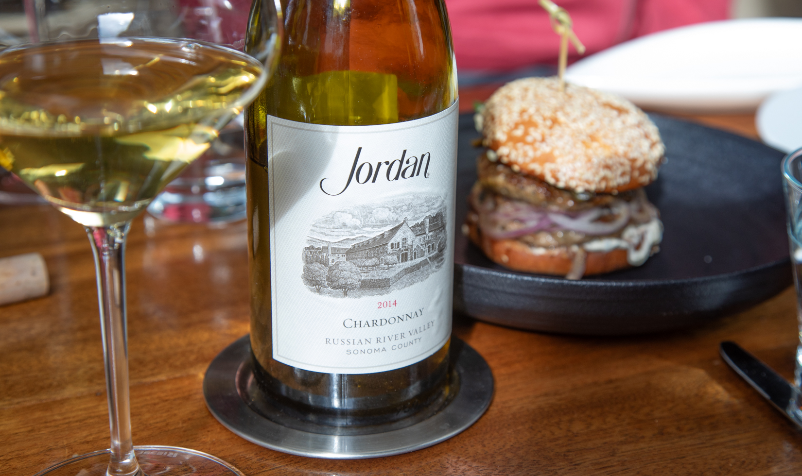 bottle of chardonnay with wine glass, wine list menu and burger on a plate in the background