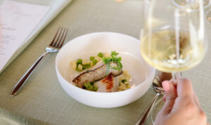 close up of halibut dinner dish inside a white bowl with a glass of white wine