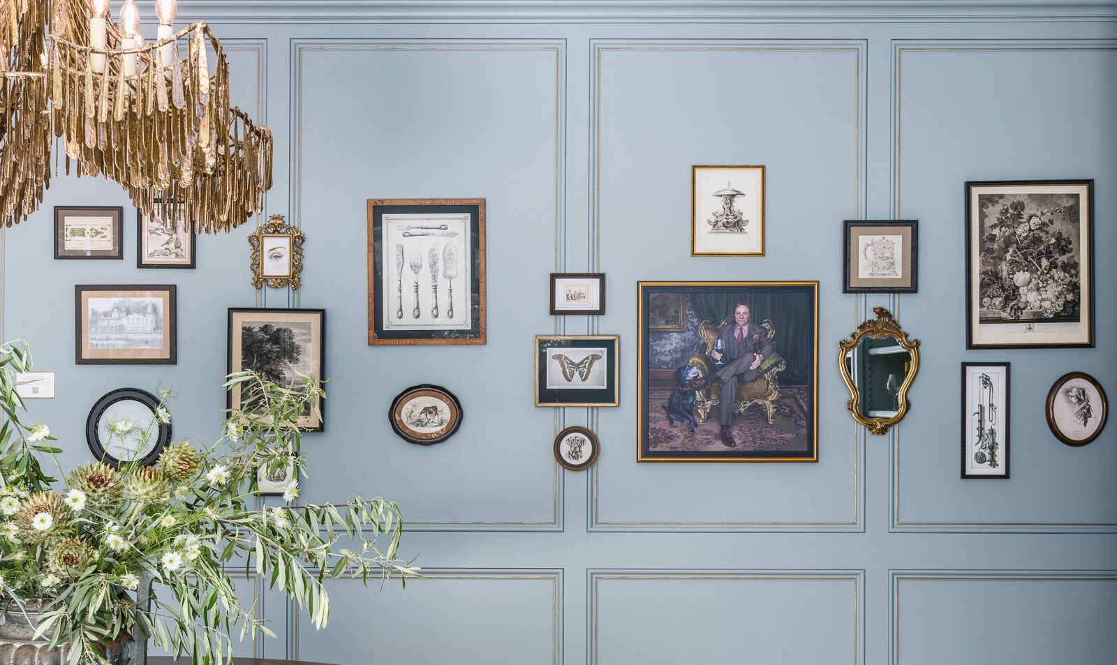 art collage of framed prints and lithographs on light blue paneled wall