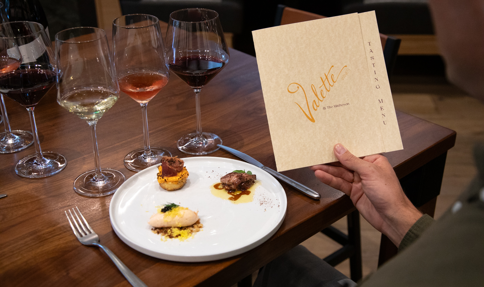 person holding menu with three appetizers and wine glasses on dinner table