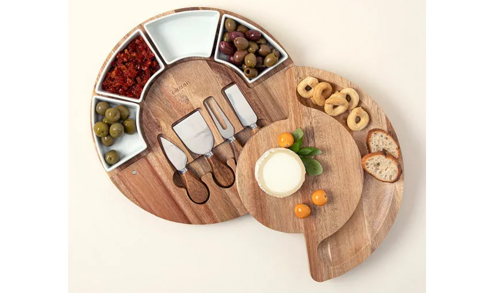 Wooden cheese board set with knives, olives, bread, and cheese.