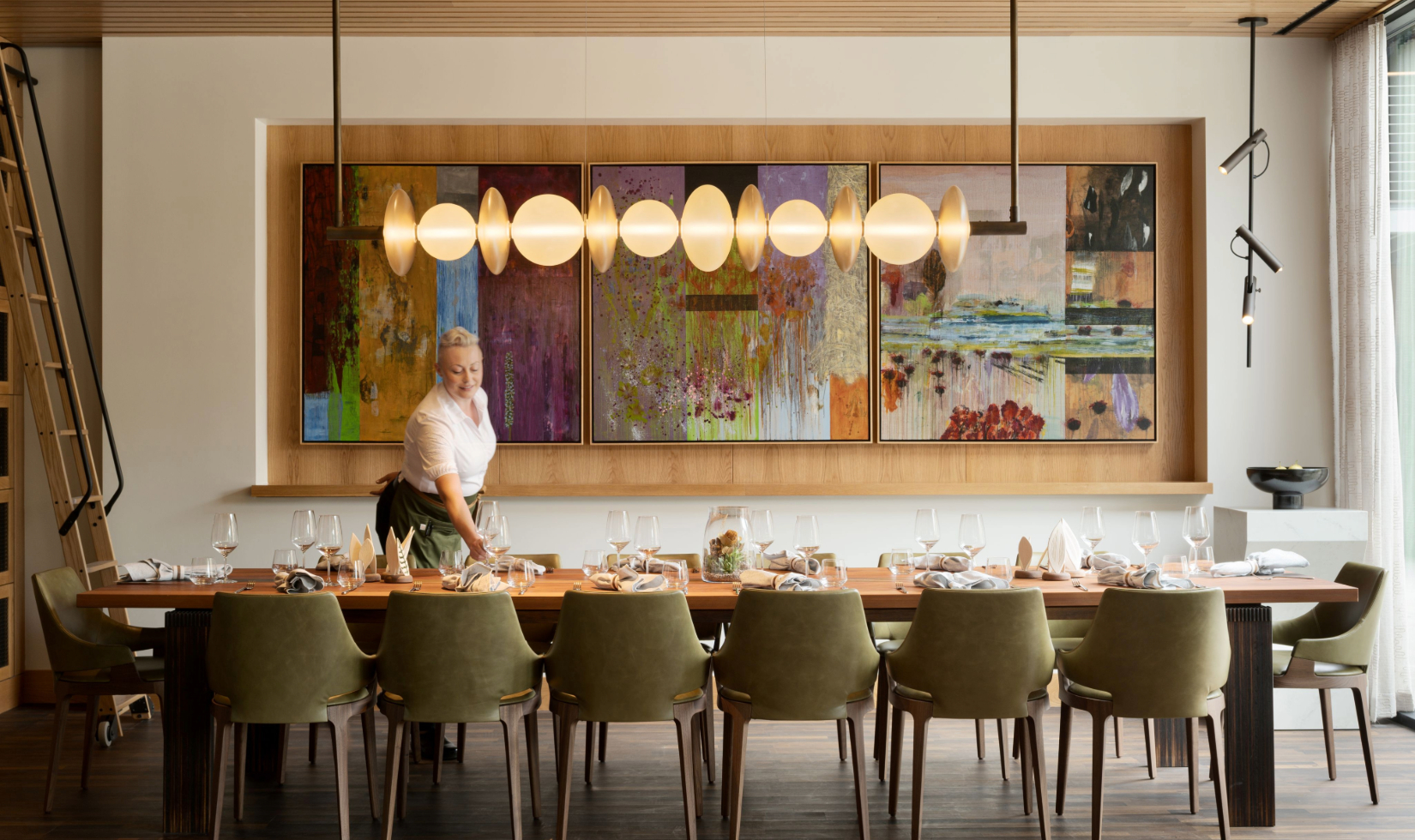 A restaurant server setting a large table in modern restaurant dining room with a large painting on the wall in the background